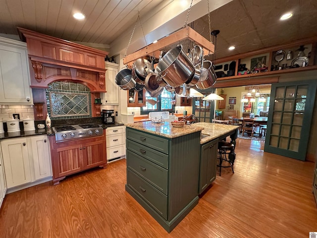 kitchen featuring pendant lighting, dark stone counters, light hardwood / wood-style floors, stainless steel gas stovetop, and a kitchen island