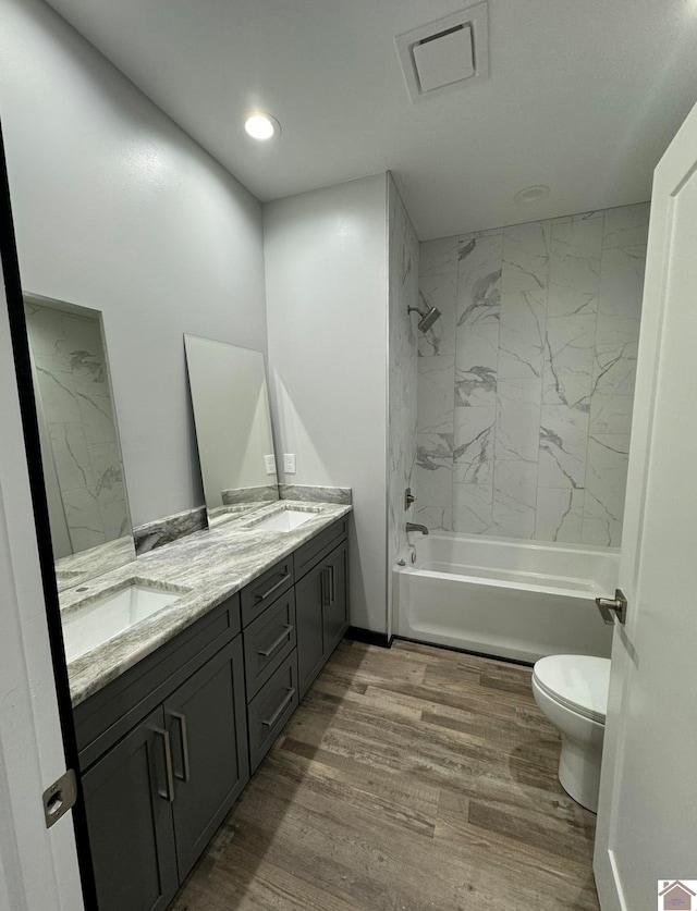 full bathroom with wood-type flooring, tiled shower / bath combo, vanity, and toilet