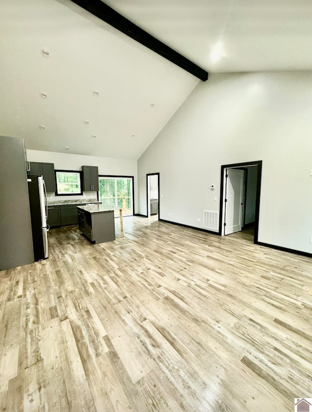 unfurnished living room featuring high vaulted ceiling, light wood-type flooring, and beam ceiling