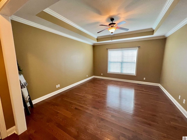 empty room with ceiling fan, a raised ceiling, dark hardwood / wood-style floors, and crown molding