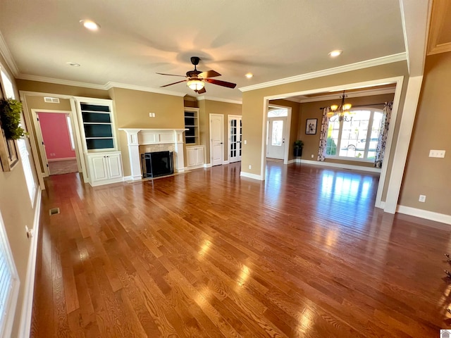 unfurnished living room with ceiling fan with notable chandelier, crown molding, built in features, and hardwood / wood-style flooring