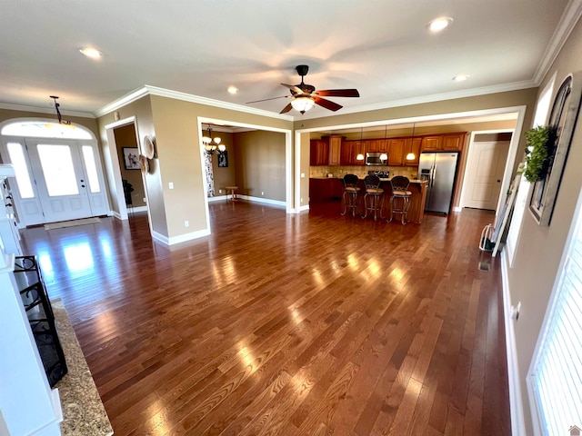 unfurnished living room featuring ceiling fan with notable chandelier, dark hardwood / wood-style floors, and ornamental molding