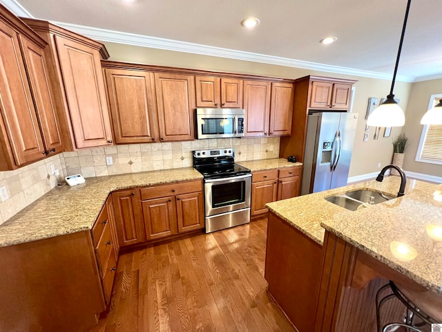 kitchen with sink, hanging light fixtures, appliances with stainless steel finishes, hardwood / wood-style floors, and ornamental molding