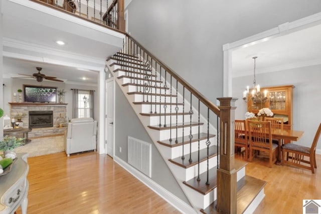 stairs featuring ceiling fan with notable chandelier, ornamental molding, hardwood / wood-style flooring, and a fireplace