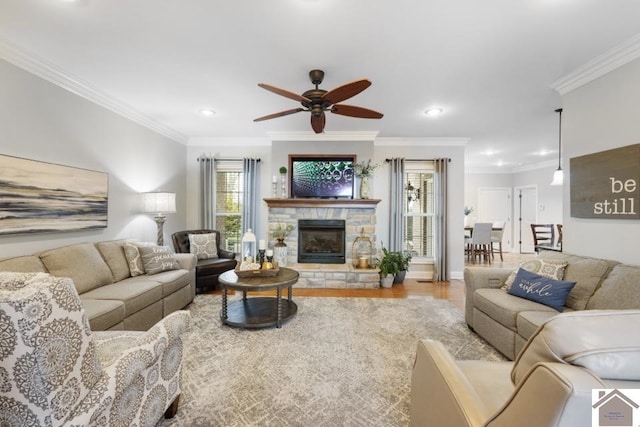 living room featuring a stone fireplace, ornamental molding, ceiling fan, and light hardwood / wood-style flooring