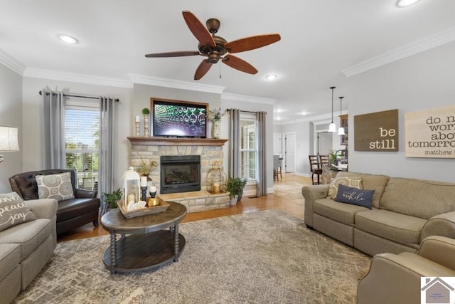 living room with ornamental molding, light hardwood / wood-style floors, ceiling fan, and a stone fireplace