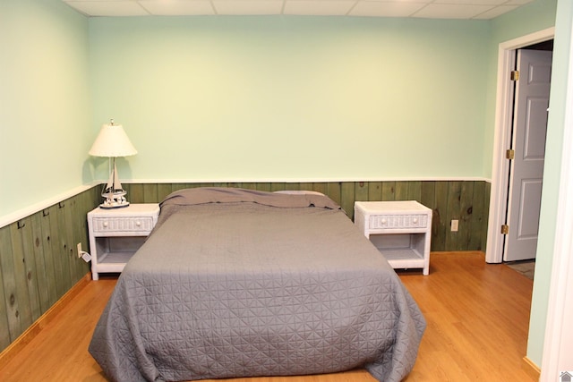 bedroom with a drop ceiling, wooden walls, and hardwood / wood-style flooring