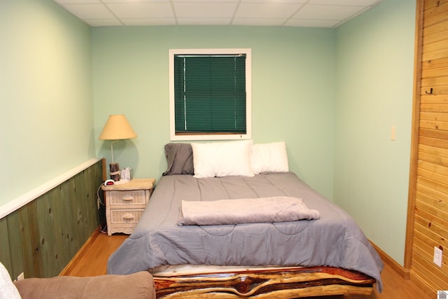 bedroom with hardwood / wood-style flooring, a drop ceiling, and wooden walls