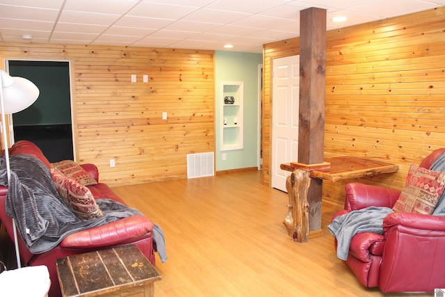 living room featuring a drop ceiling, wood walls, and light hardwood / wood-style floors