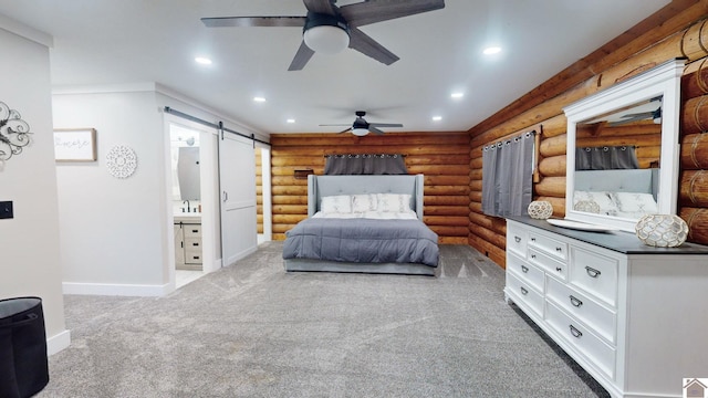 carpeted bedroom with rustic walls, ensuite bathroom, ceiling fan, and a barn door