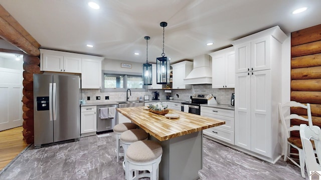 kitchen with pendant lighting, white cabinets, a kitchen island, custom range hood, and appliances with stainless steel finishes