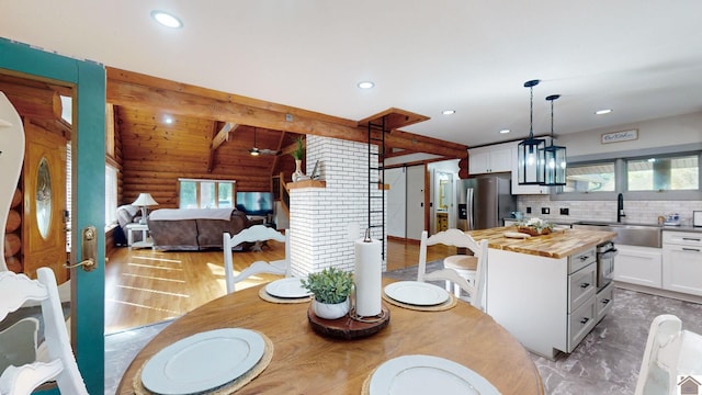 dining room featuring beam ceiling, sink, light hardwood / wood-style flooring, and a wealth of natural light