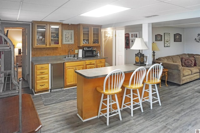 kitchen featuring sink, dark wood-type flooring, stainless steel refrigerator, a drop ceiling, and a kitchen breakfast bar