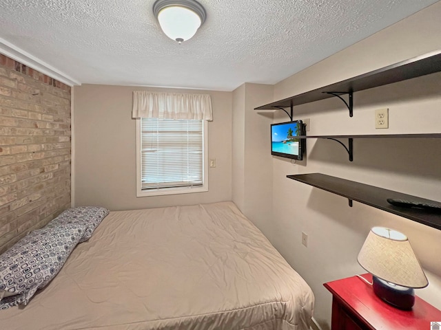 bedroom featuring a textured ceiling and brick wall