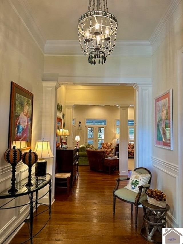 hall with a notable chandelier, dark wood-type flooring, crown molding, and ornate columns