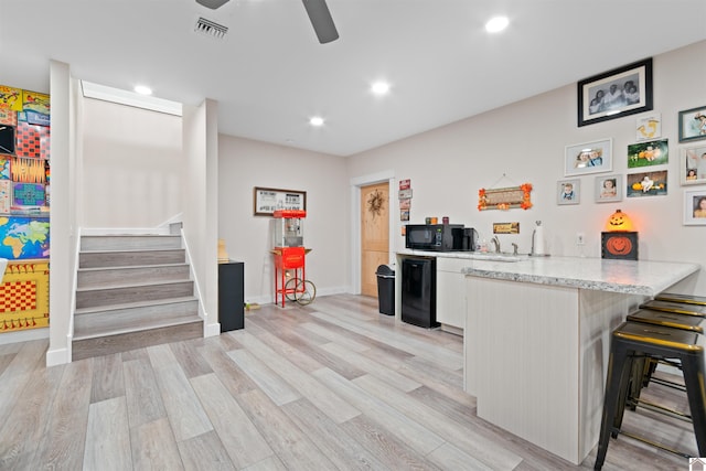 kitchen with light hardwood / wood-style floors, white cabinets, kitchen peninsula, a breakfast bar area, and ceiling fan