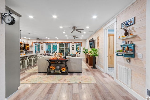 living room featuring bar area, wooden walls, light wood-type flooring, and ornamental molding