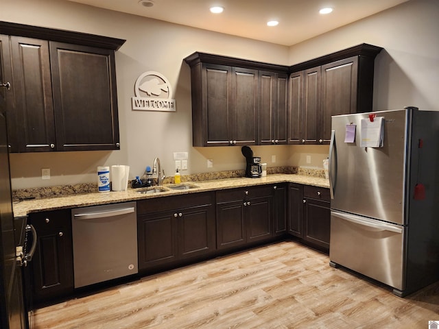 kitchen with dark brown cabinets, light stone counters, sink, light hardwood / wood-style flooring, and appliances with stainless steel finishes