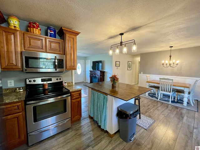 kitchen featuring wood-type flooring, a textured ceiling, a notable chandelier, appliances with stainless steel finishes, and decorative light fixtures