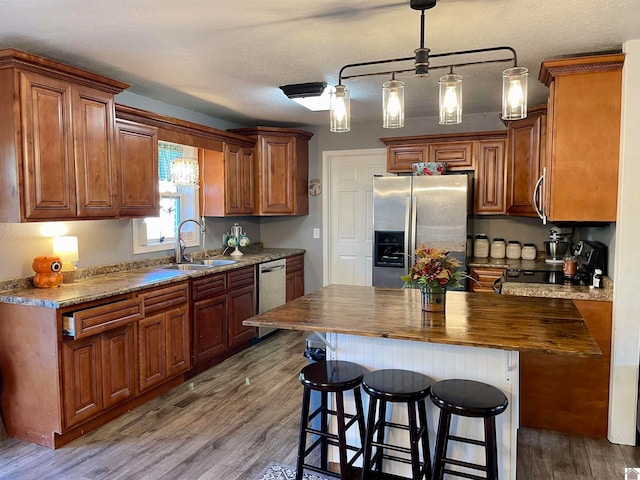 kitchen featuring sink, a kitchen island, a textured ceiling, hardwood / wood-style flooring, and appliances with stainless steel finishes