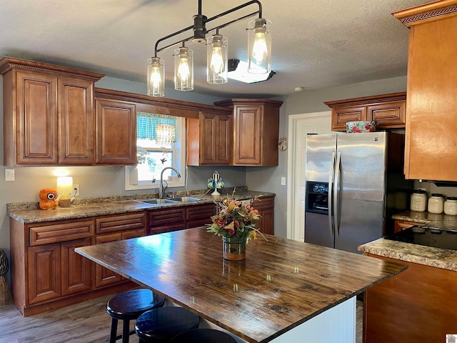 kitchen with hanging light fixtures, a textured ceiling, wood-type flooring, stainless steel refrigerator with ice dispenser, and sink