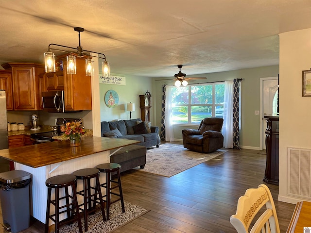 kitchen featuring ceiling fan with notable chandelier, a kitchen bar, stainless steel appliances, decorative light fixtures, and dark hardwood / wood-style flooring