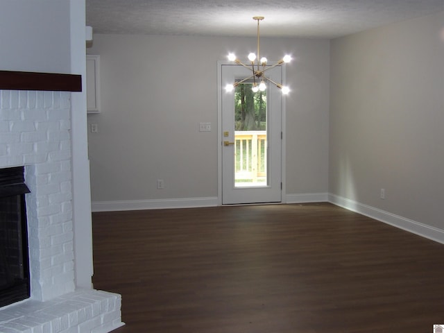 unfurnished living room featuring dark wood-type flooring, a brick fireplace, a chandelier, and a textured ceiling