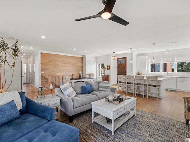 living room with wood-type flooring, wooden walls, sink, and ceiling fan