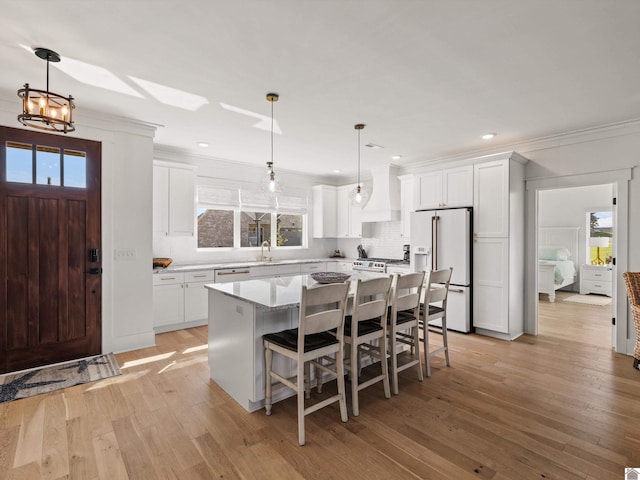 kitchen featuring high end white fridge, white cabinets, hanging light fixtures, a kitchen island, and light hardwood / wood-style flooring