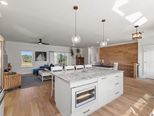 kitchen featuring white cabinetry, a breakfast bar, stainless steel microwave, a kitchen island, and light hardwood / wood-style flooring