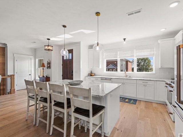 kitchen featuring light wood-type flooring, white cabinetry, a center island, and decorative light fixtures