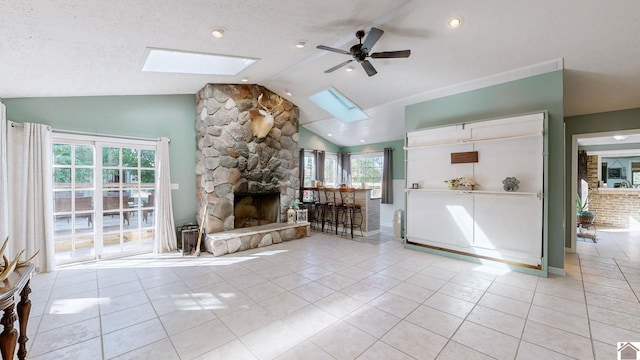 unfurnished living room featuring a textured ceiling, a stone fireplace, light tile patterned floors, lofted ceiling with skylight, and ceiling fan