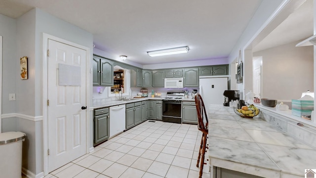 kitchen with tile counters, white appliances, sink, and light tile patterned floors