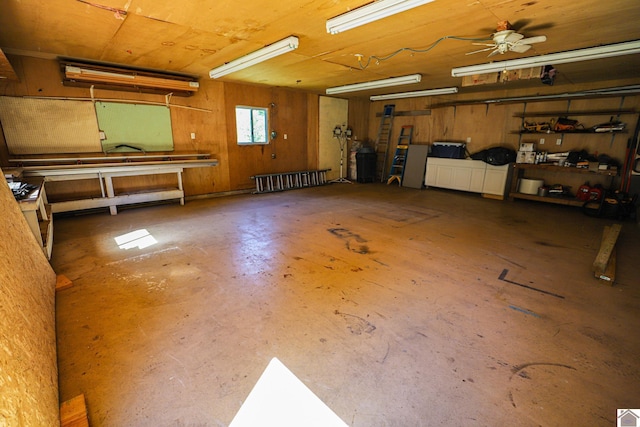 garage featuring ceiling fan, wooden walls, and a workshop area