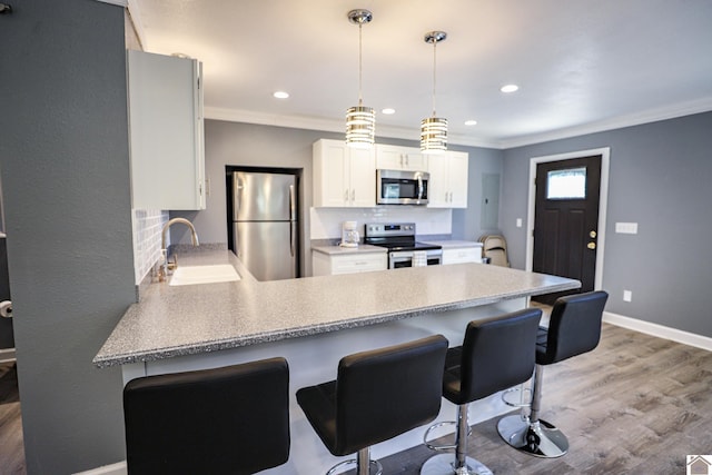 kitchen featuring appliances with stainless steel finishes, a breakfast bar, white cabinets, kitchen peninsula, and sink