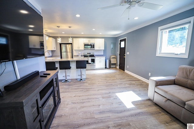 living room featuring light wood-type flooring, crown molding, sink, and ceiling fan