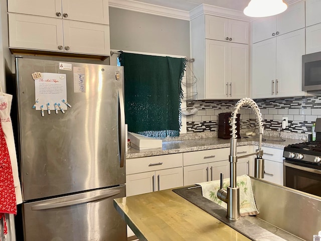 kitchen featuring light stone counters, white cabinets, stainless steel appliances, and backsplash