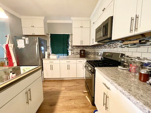 kitchen with white cabinets, backsplash, appliances with stainless steel finishes, light wood-type flooring, and crown molding