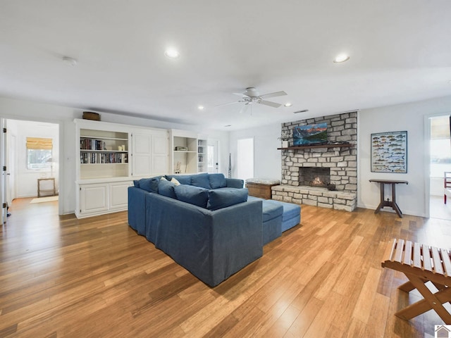 living room with ceiling fan, light hardwood / wood-style flooring, a large fireplace, and a wealth of natural light