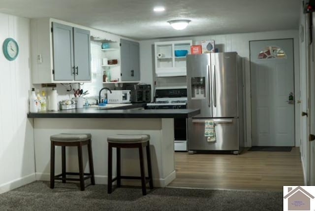 kitchen with kitchen peninsula, wood-type flooring, stainless steel refrigerator with ice dispenser, white stove, and a breakfast bar