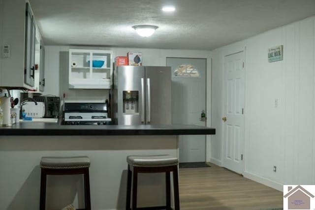 kitchen featuring white cabinets, kitchen peninsula, range, stainless steel fridge with ice dispenser, and a breakfast bar area