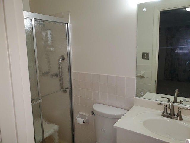 bathroom with vanity, tile walls, toilet, and a shower with shower door