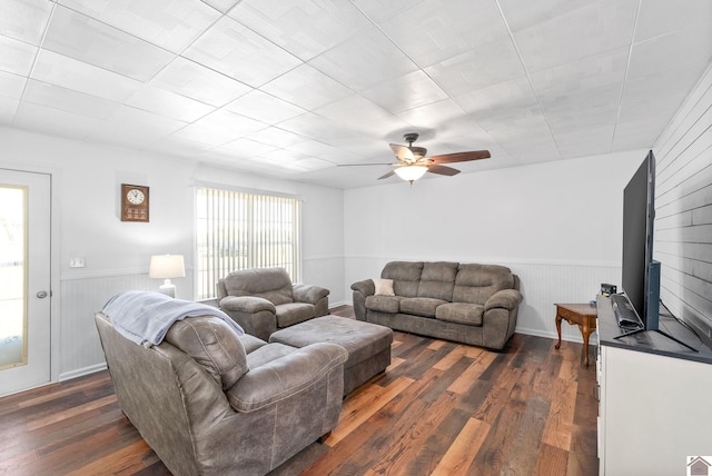 living room featuring dark hardwood / wood-style floors, wooden walls, and ceiling fan