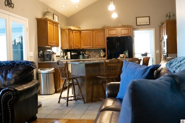 kitchen featuring light wood-type flooring, tasteful backsplash, decorative light fixtures, black fridge, and a kitchen bar