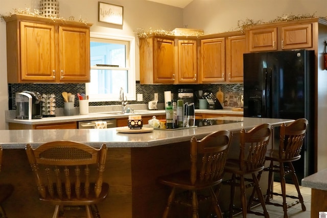 kitchen featuring decorative backsplash, black fridge, a breakfast bar area, and sink