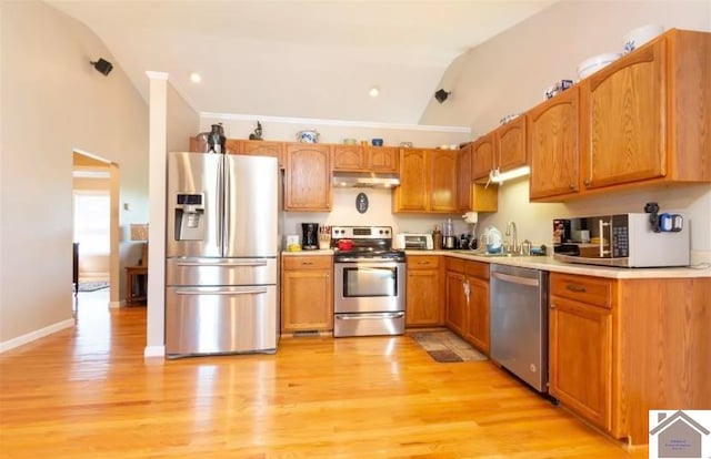 kitchen featuring appliances with stainless steel finishes, lofted ceiling, sink, and light wood-type flooring