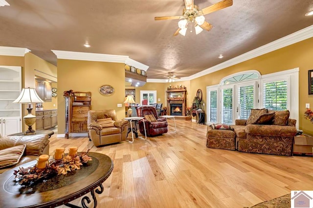 living room featuring ceiling fan, ornamental molding, a textured ceiling, and light wood-type flooring