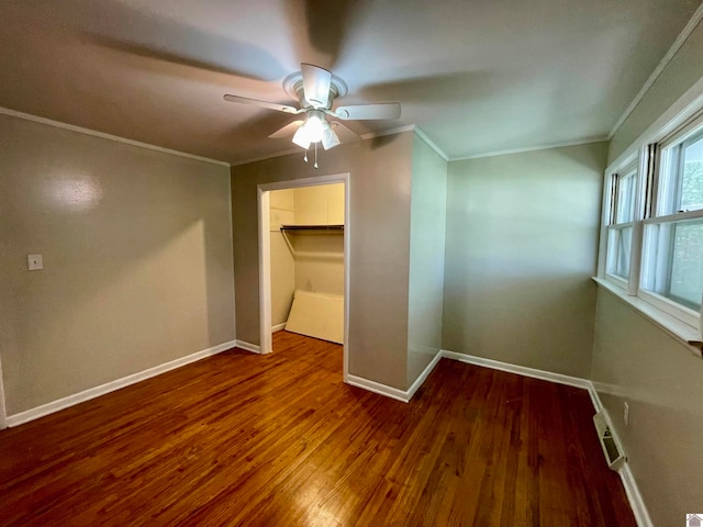 unfurnished bedroom featuring ceiling fan, a walk in closet, a closet, crown molding, and hardwood / wood-style floors