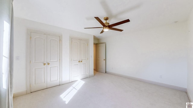 unfurnished bedroom featuring light carpet, two closets, and ceiling fan