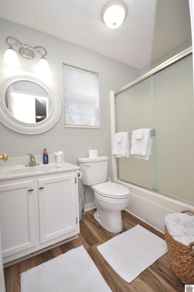 full bathroom with vanity, toilet, wood-type flooring, and bath / shower combo with glass door